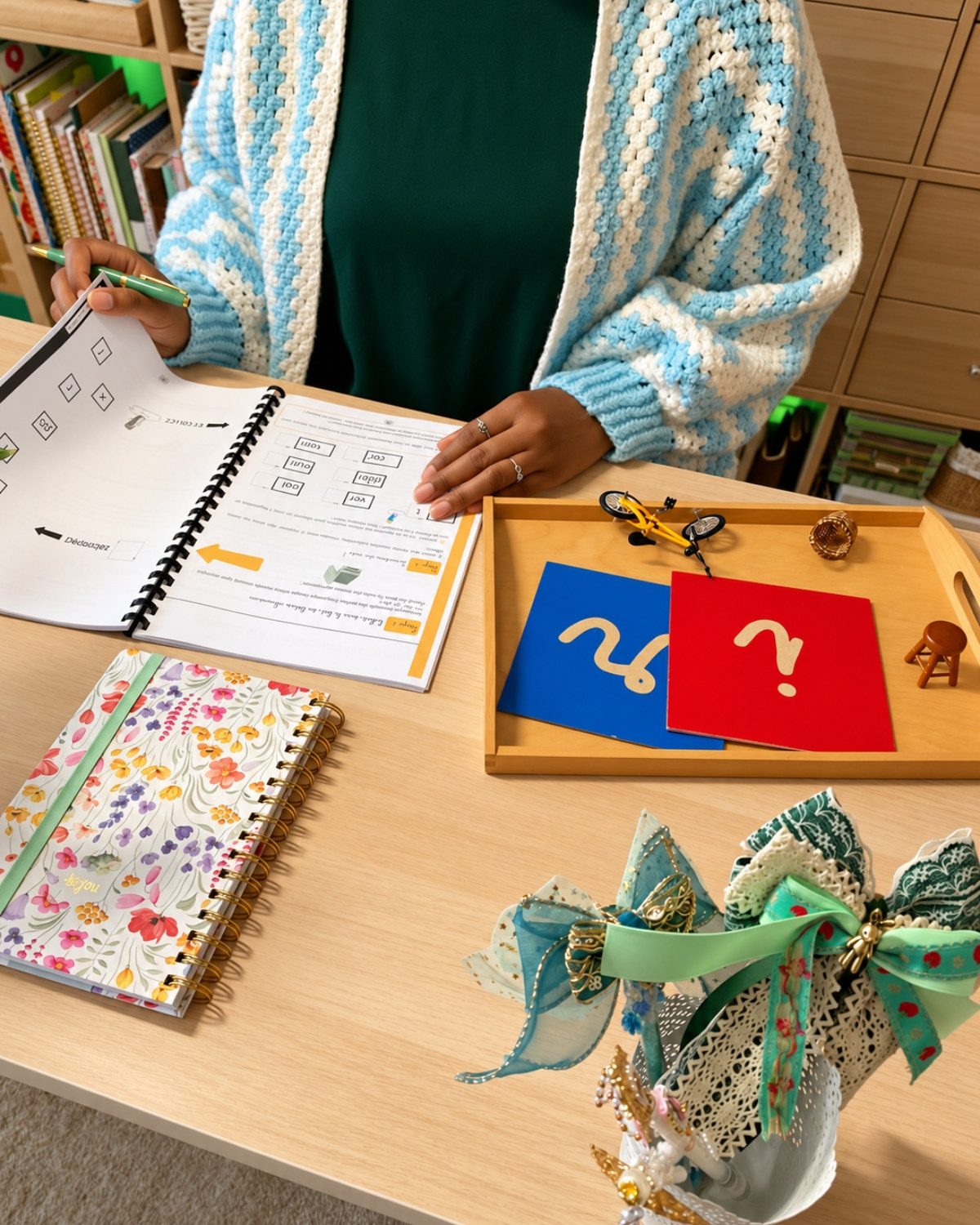 Alima à sa table de travail, un cahier pratique ouvert et des lettres rugueuses Montessori sur un plateau