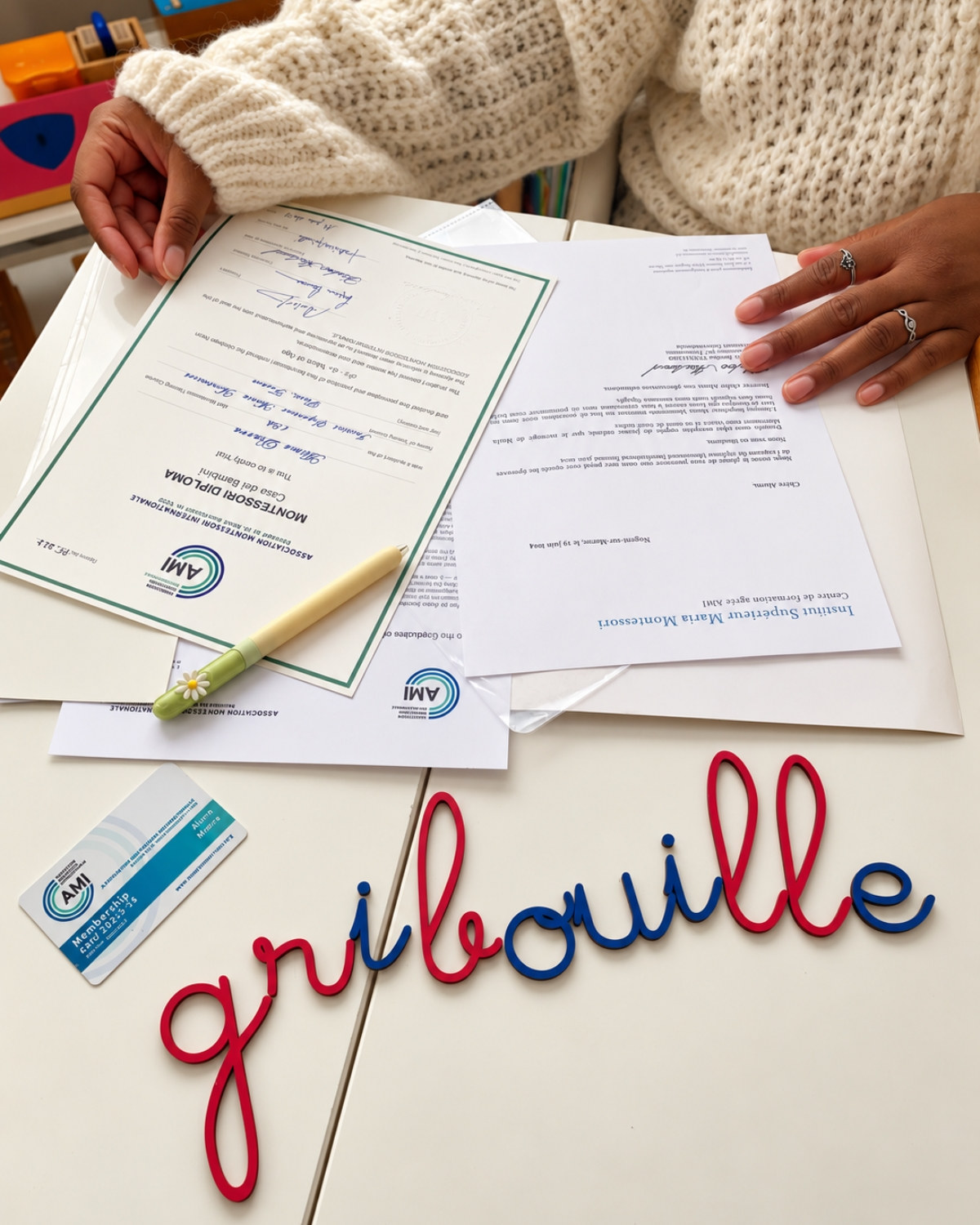 Le diplôme Montessori AMI d'Alima, sa carte de membre AMI et le mot gribouille en lettres rouges et bleues
