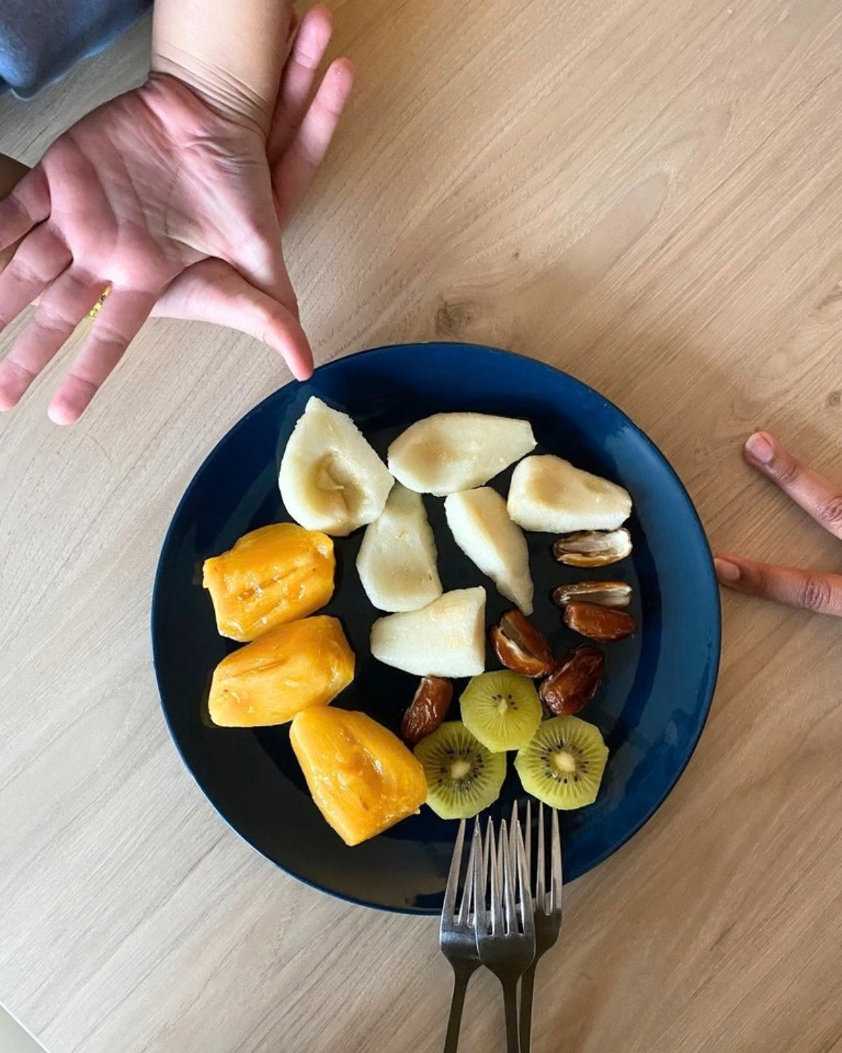 Des mains d'enfants autour d'une assiette de fruits et de dattes