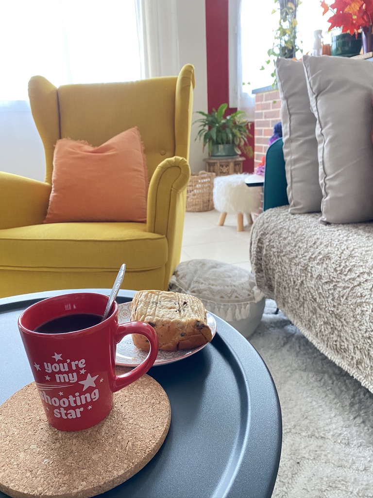 Un café et une part de cake sur la table du salon, près du fauteuil jaune